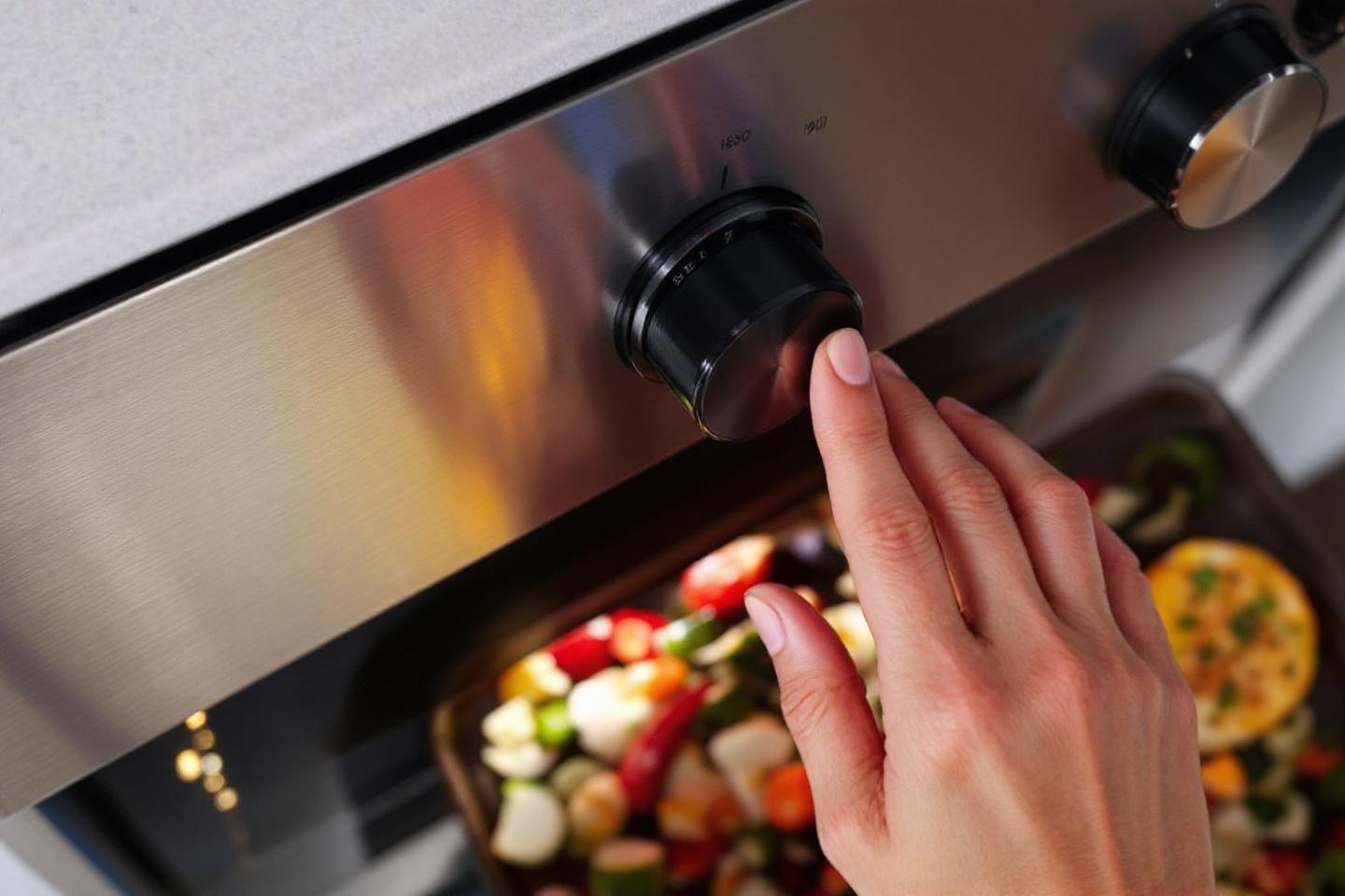Main ajustant le bouton de temp&eacute;rature d'un four avec l&eacute;gumes