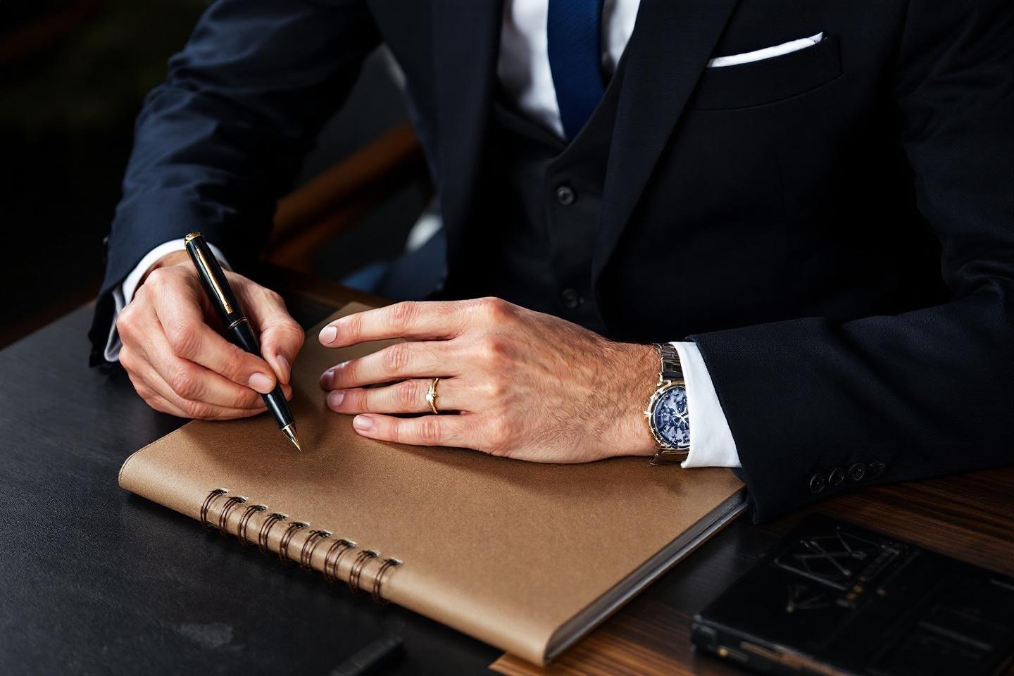 Main avec stylo et montre, &eacute;crivant dans un carnet marron