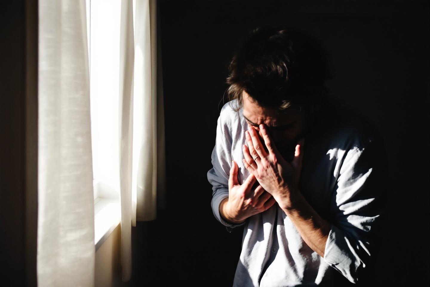 Personne effondrée, visage caché par les mains, près d'un rideau