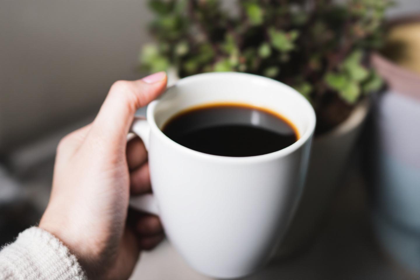 Main tenant une tasse de caf&eacute; noir pr&egrave;s d'une plante