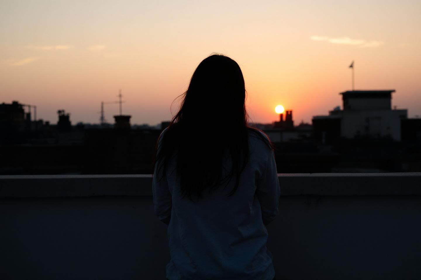 Personne de dos observant un coucher de soleil urbain