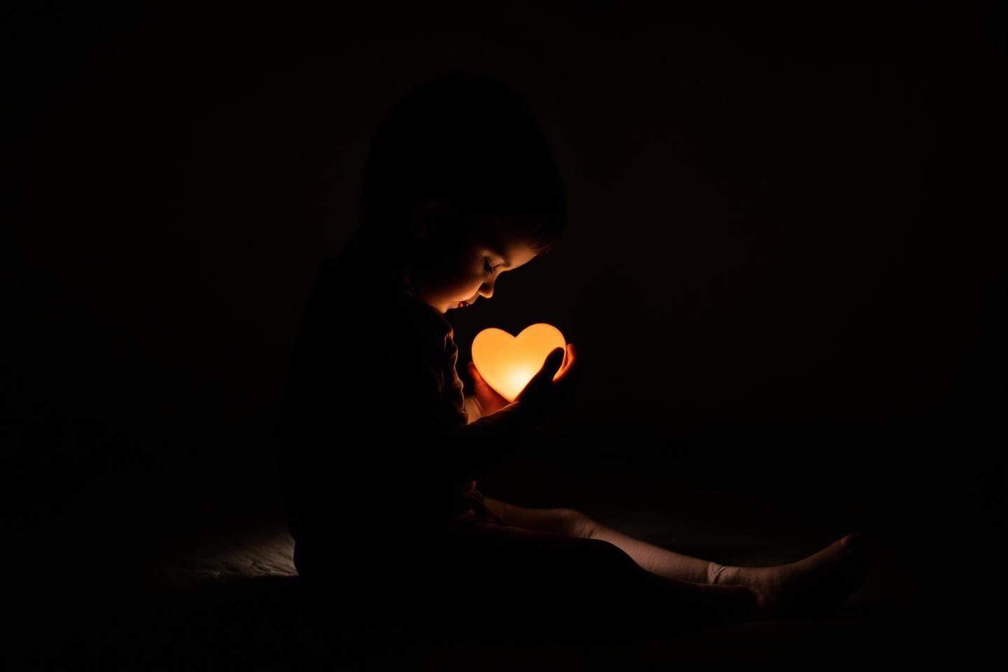 Main tenant un cœur brillant dans un environnement sombre