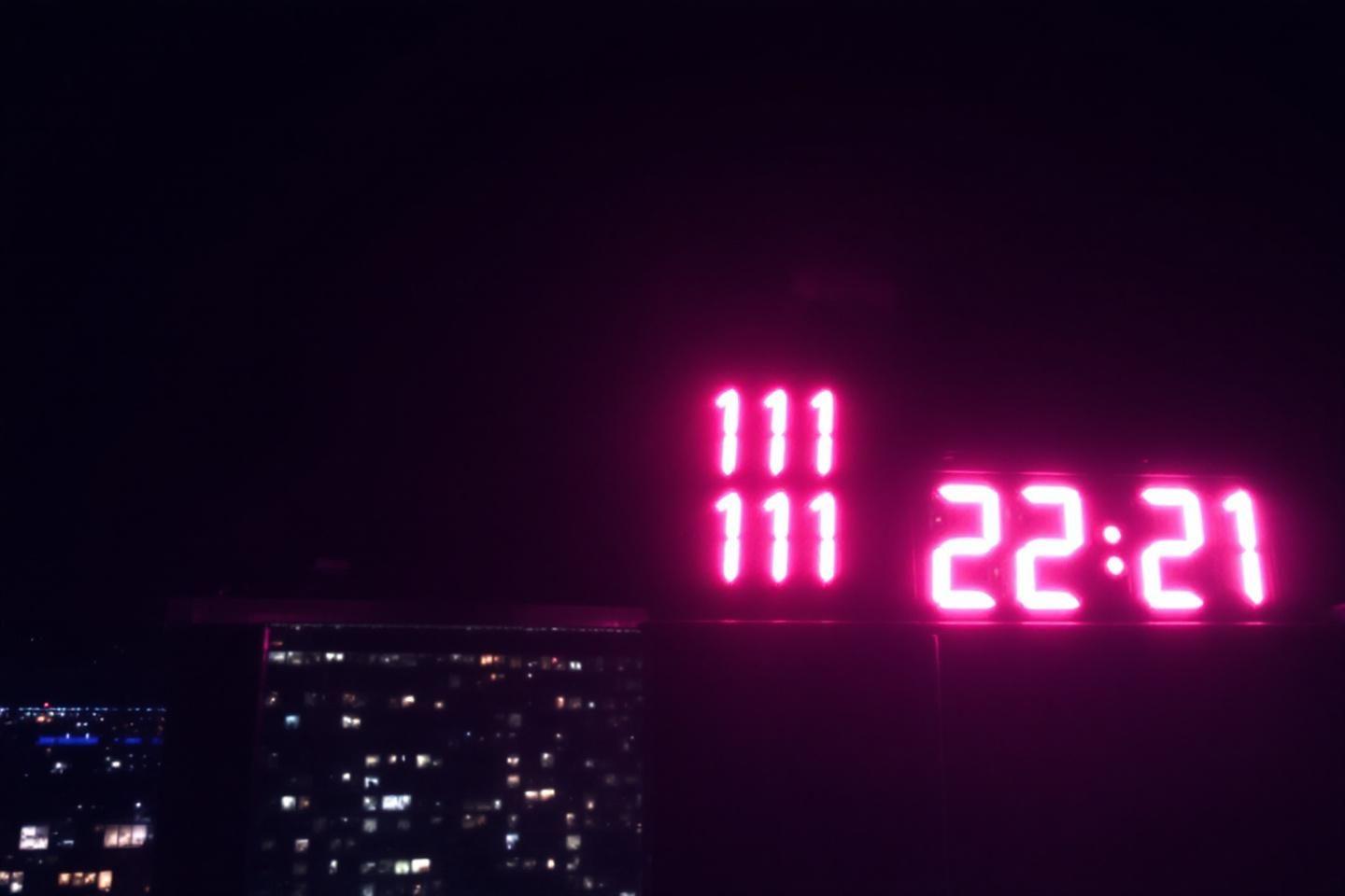 Horloge rose vif affichant 22:21 avec vue sur ville la nuit