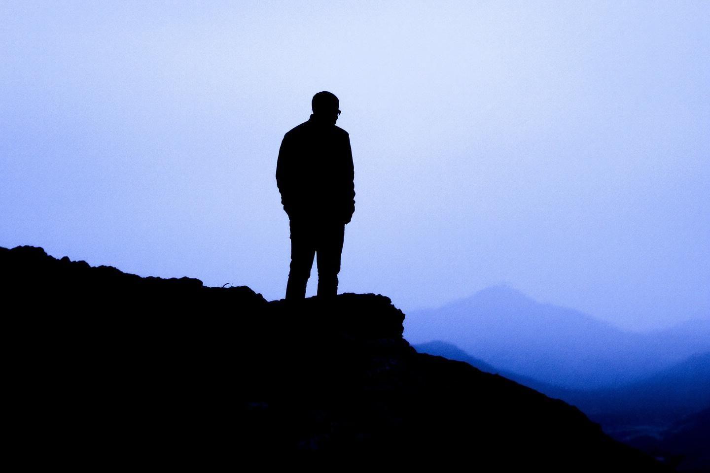 Silhouette d'une personne sur un rocher face à des montagnes brumeuses